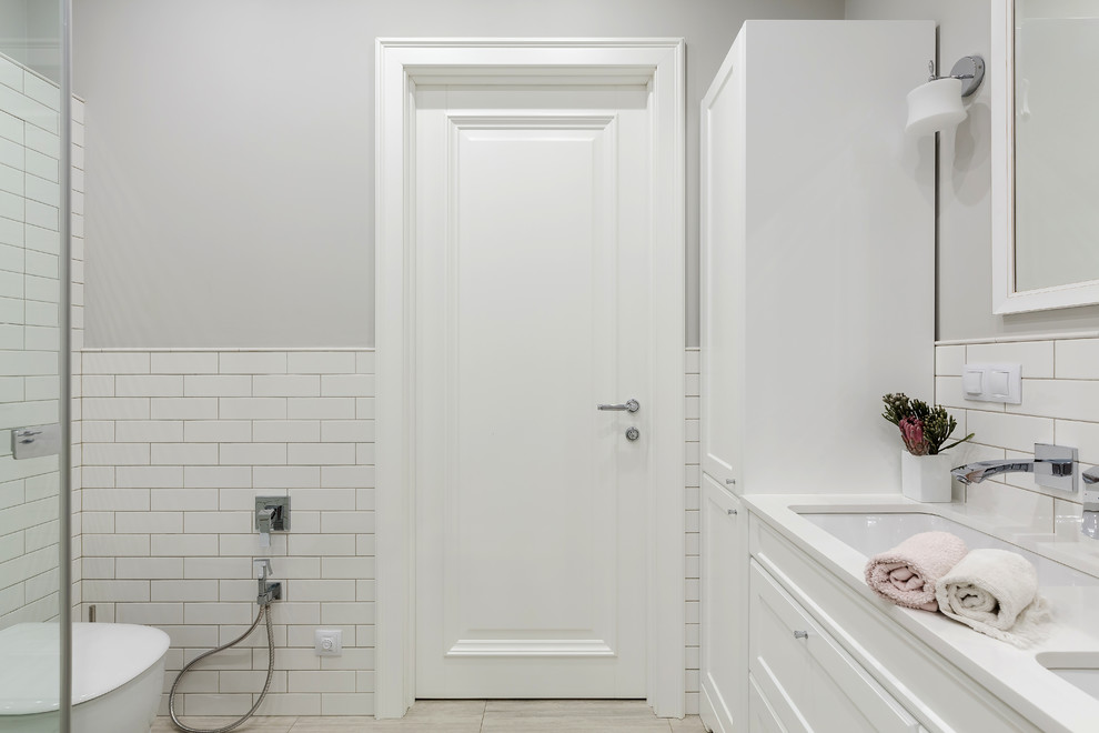 Идея дизайна: большая ванная комната в стиле неоклассика (современная классика) с фасадами с утопленной филенкой, инсталляцией, белой плиткой, серыми стенами, врезной раковиной, столешницей из искусственного кварца, белой столешницей и белыми фасадами