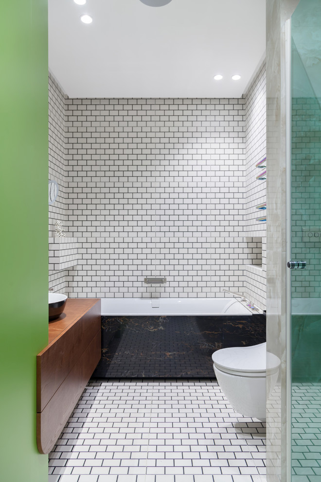Exempel på ett modernt en-suite badrum, med släta luckor, skåp i mellenmörkt trä, ett badkar i en alkov, en dusch i en alkov, en vägghängd toalettstol, vit kakel, ett fristående handfat och vitt golv