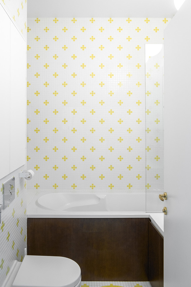 Bild på ett litet funkis en-suite badrum, med släta luckor, skåp i mellenmörkt trä, ett badkar i en alkov, en dusch/badkar-kombination, en toalettstol med separat cisternkåpa, vit kakel, gul kakel och flerfärgat golv