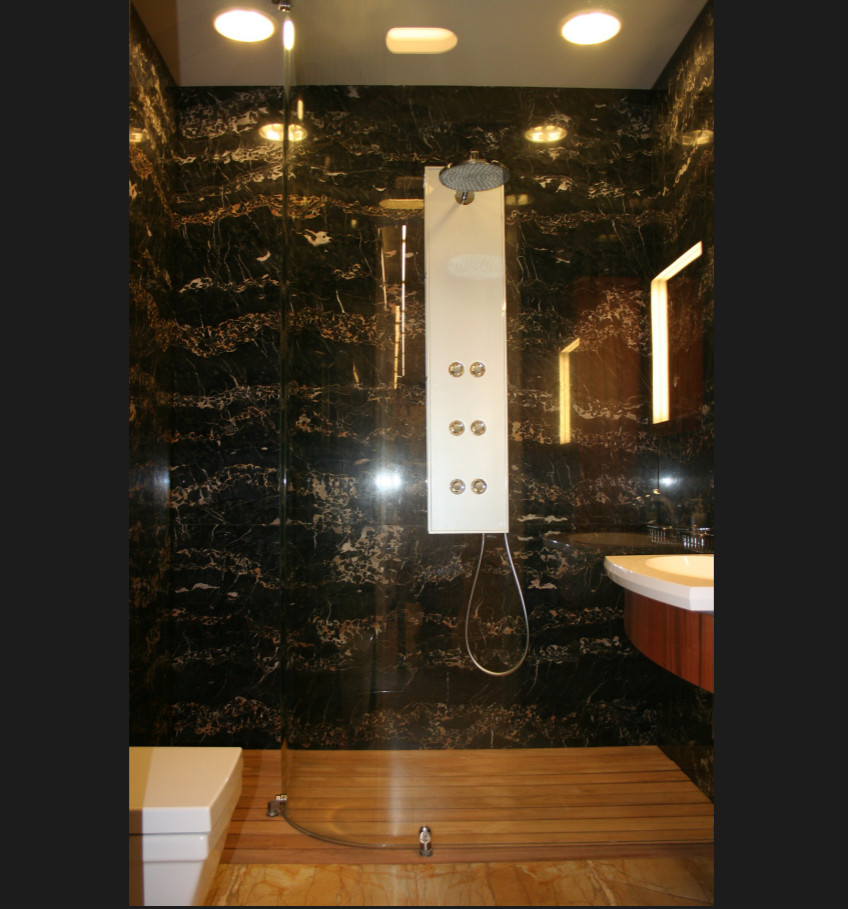 Modern inredning av ett mellanstort vit vitt badrum med dusch, med släta luckor, skåp i mellenmörkt trä, en kantlös dusch, en toalettstol med hel cisternkåpa, svart kakel, stenhäll, svarta väggar, kalkstensgolv, ett konsol handfat, bänkskiva i akrylsten, gult golv och med dusch som är öppen
