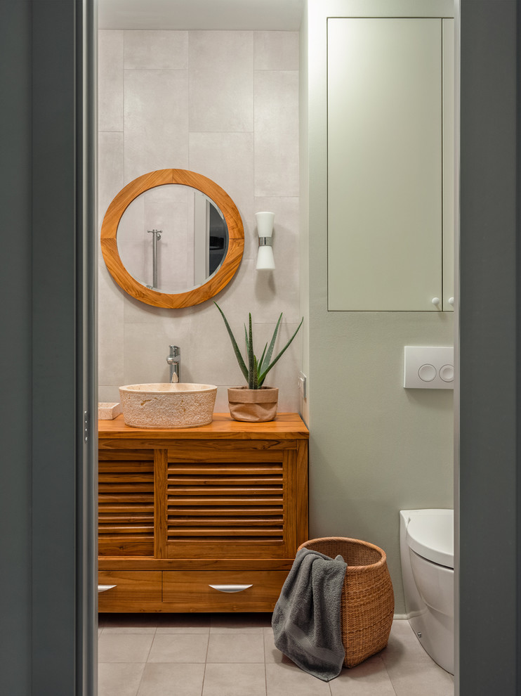 Foto på ett mellanstort eklektiskt brun en-suite badrum, med luckor med lamellpanel, skåp i mellenmörkt trä, ett badkar i en alkov, en vägghängd toalettstol, grå kakel, keramikplattor, gröna väggar, klinkergolv i porslin, ett nedsänkt handfat, träbänkskiva och grått golv