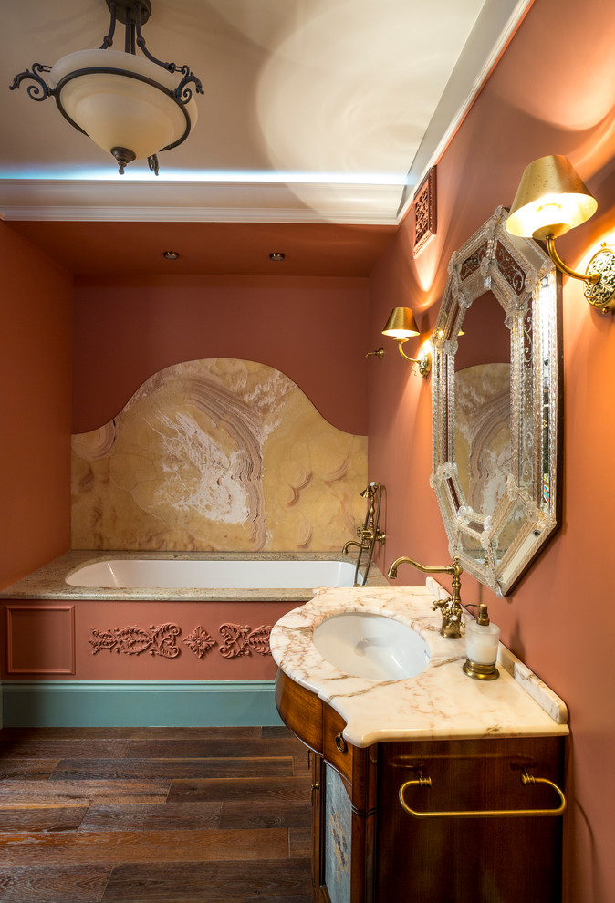 Idée de décoration pour une salle de bain principale bohème en bois foncé avec une baignoire encastrée, un carrelage jaune, des dalles de pierre, un mur orange, un lavabo encastré et un plan de toilette en marbre.