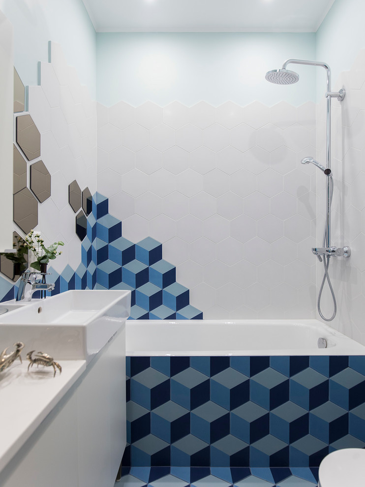 Cette photo montre une petite salle de bain principale tendance avec un placard à porte plane, des portes de placard blanches, un carrelage bleu, un carrelage blanc, des carreaux de porcelaine, un mur blanc, un sol en carrelage de céramique, un plan de toilette en surface solide, un sol bleu, une baignoire en alcôve, un combiné douche/baignoire et une vasque.