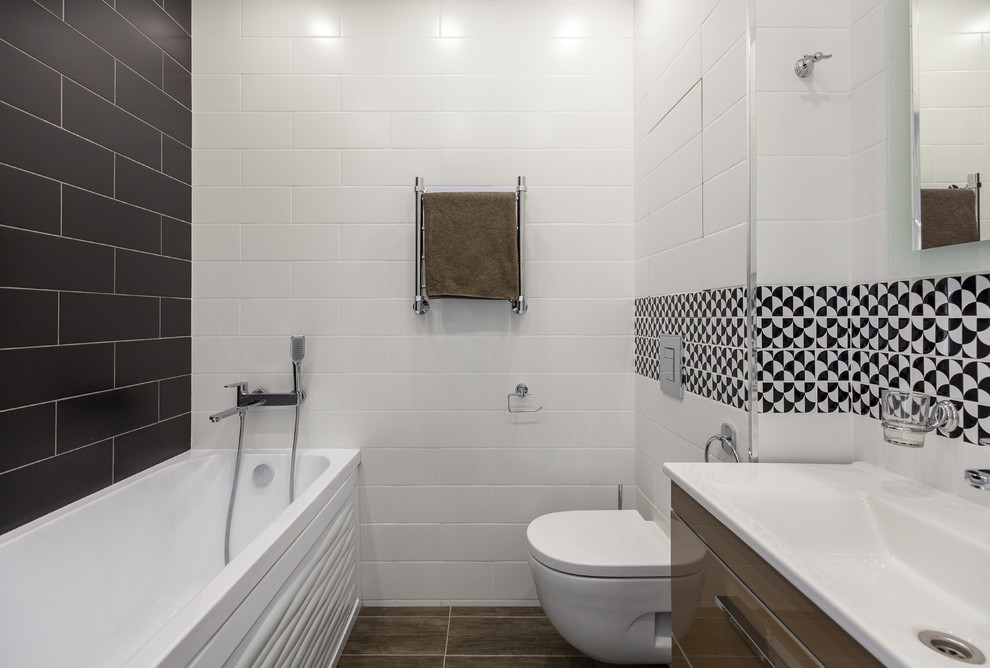 Exemple d'une salle de bain principale scandinave avec un placard à porte plane, des portes de placard marrons, une baignoire en alcôve, un combiné douche/baignoire, WC suspendus, un carrelage blanc, un carrelage noir et blanc, un lavabo intégré et un sol marron.