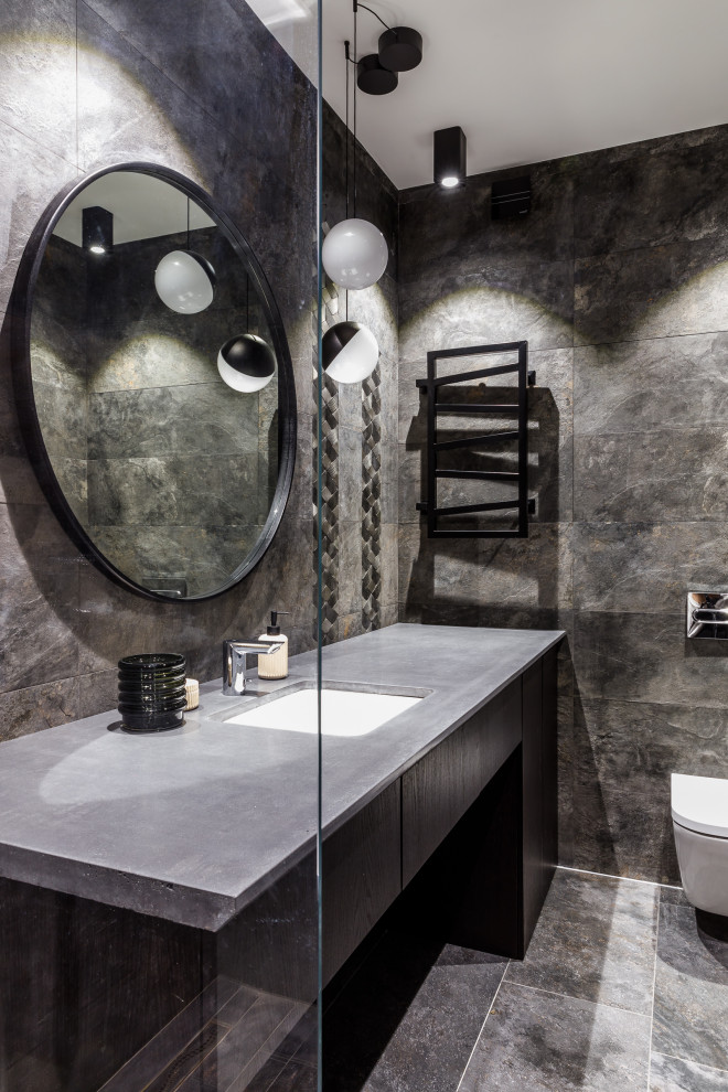 Bild på ett funkis grå grått badrum med dusch, med släta luckor, svarta skåp, en vägghängd toalettstol, grå kakel, ett undermonterad handfat och grått golv