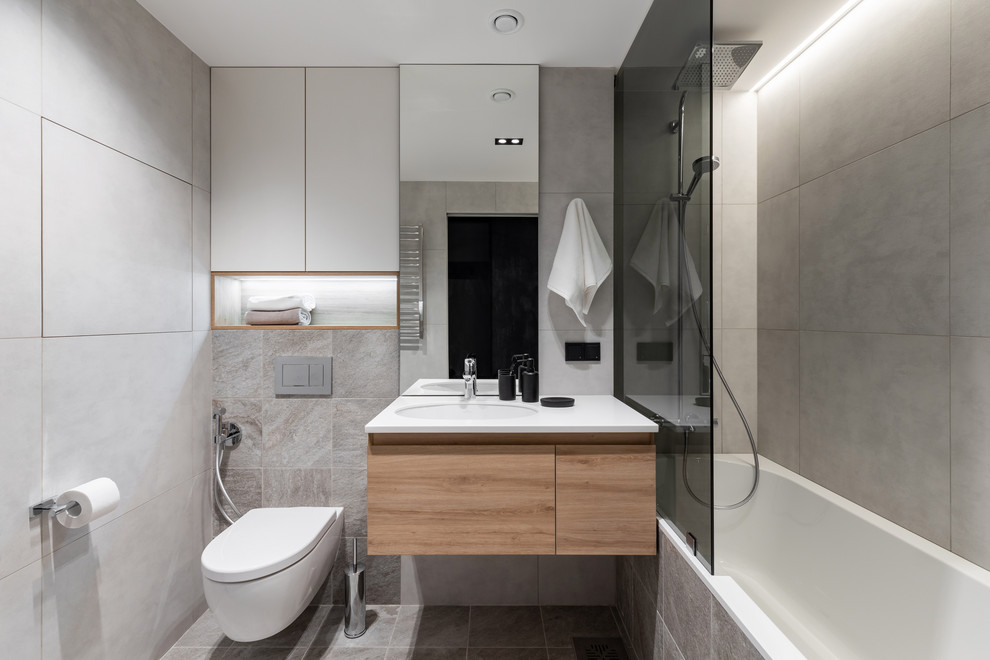 Пример оригинального дизайна: главная ванная комната в современном стиле с плоскими фасадами, ванной в нише, душем над ванной, инсталляцией, серой плиткой, врезной раковиной, серым полом, белой столешницей, светлыми деревянными фасадами, серыми стенами, тумбой под одну раковину и подвесной тумбой