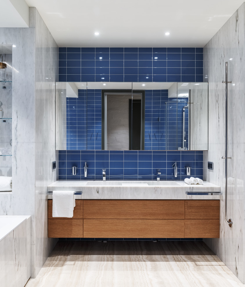 Идея дизайна: большая детская ванная комната в современном стиле с плоскими фасадами, фасадами цвета дерева среднего тона, полновстраиваемой ванной, угловым душем, инсталляцией, синей плиткой, керамической плиткой, синими стенами, полом из травертина, раковиной с несколькими смесителями, мраморной столешницей, бежевым полом, душем с распашными дверями, белой столешницей и акцентной стеной