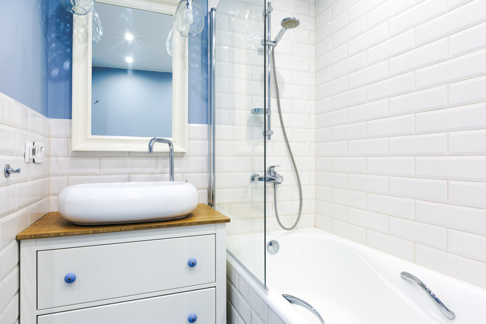 Diseño de cuarto de baño escandinavo pequeño con armarios con paneles lisos, puertas de armario blancas, combinación de ducha y bañera, encimera de madera, baldosas y/o azulejos blancos, baldosas y/o azulejos de cemento, paredes azules y lavabo sobreencimera