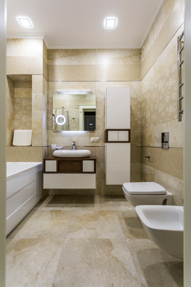 Пример оригинального дизайна: ванная комната в современном стиле с плоскими фасадами, белыми фасадами, накладной ванной, биде, бежевой плиткой, бежевыми стенами, настольной раковиной, столешницей из дерева, бежевым полом и коричневой столешницей