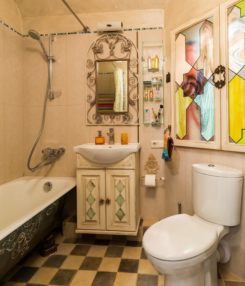 На фото: маленькая ванная комната в средиземноморском стиле с фасадами с выступающей филенкой, ванной на ножках, бежевой плиткой, керамической плиткой, полом из керамической плитки, накладной раковиной, искусственно-состаренными фасадами, душем над ванной, раздельным унитазом и бежевыми стенами для на участке и в саду