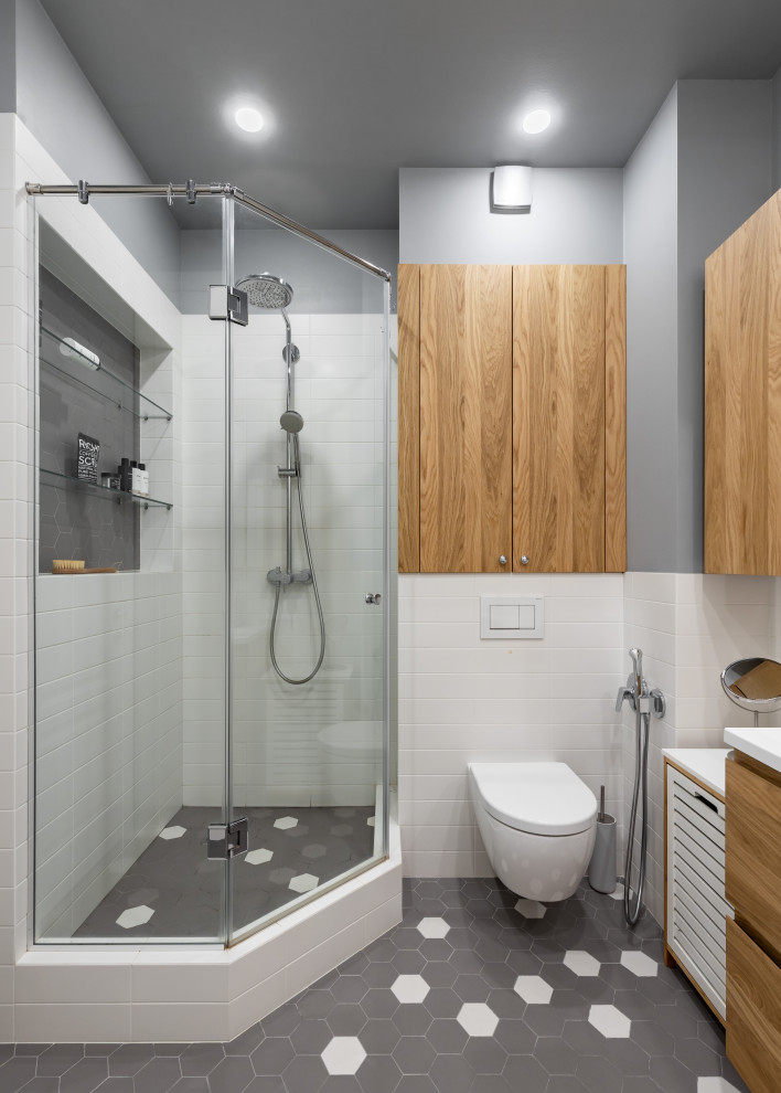 Réalisation d'une salle de bain nordique de taille moyenne avec un placard à porte plane, des portes de placard marrons, une baignoire en alcôve, une douche d'angle, WC suspendus, un carrelage blanc, des carreaux de céramique, un mur gris, un sol en carrelage de céramique, un lavabo de ferme, un plan de toilette en surface solide, un sol gris, une cabine de douche à porte coulissante et un plan de toilette blanc.