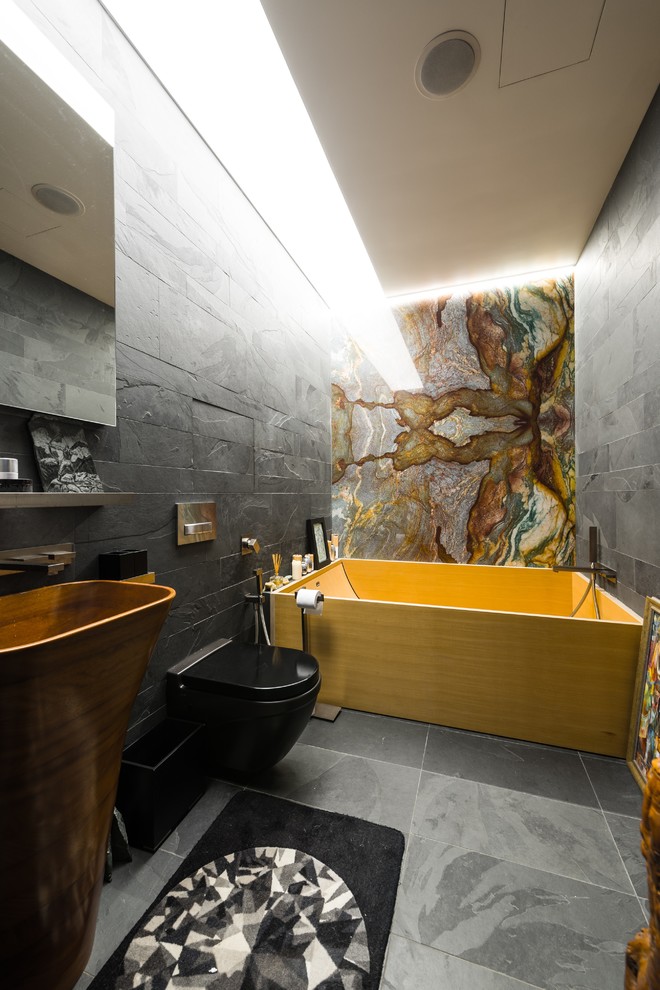 Inspiration for a contemporary ensuite bathroom in Moscow with a wall mounted toilet, grey tiles, a freestanding bath, grey walls, a pedestal sink, grey floors and a feature wall.