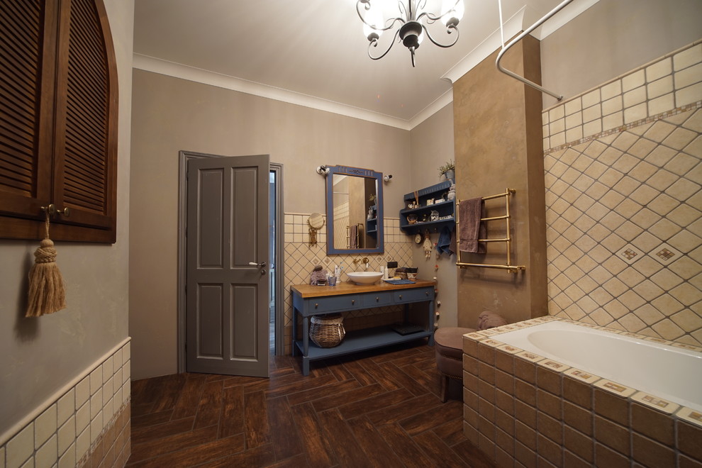 Inredning av ett lantligt stort gul gult en-suite badrum, med en dusch/badkar-kombination, beige kakel, porslinskakel, klinkergolv i porslin, blå skåp, ett undermonterat badkar, en vägghängd toalettstol, beige väggar, ett nedsänkt handfat, träbänkskiva, brunt golv och släta luckor