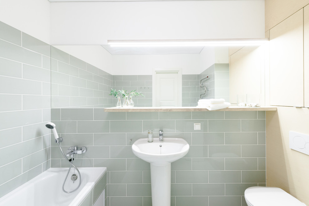 Стильный дизайн: ванная комната в скандинавском стиле с ванной в нише, душем над ванной, серой плиткой и раковиной с пьедесталом - последний тренд