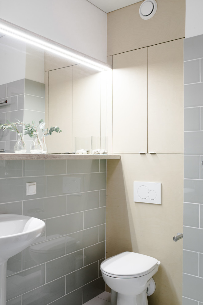Skandinavisk inredning av ett badrum, med en toalettstol med separat cisternkåpa, grå kakel, vita väggar och ett piedestal handfat