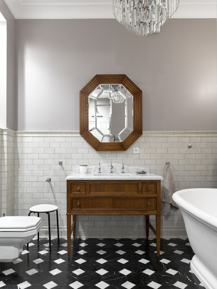 Cette photo montre une salle de bain principale chic en bois brun avec un placard avec porte à panneau encastré, une baignoire indépendante, WC suspendus, un mur gris, un lavabo encastré, un plan de toilette en marbre, un sol noir et un carrelage gris.