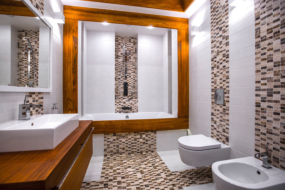На фото: главная ванная комната в современном стиле с плоскими фасадами, фасадами цвета дерева среднего тона, ванной в нише, душем над ванной, инсталляцией, бежевой плиткой, белой плиткой, настольной раковиной и бежевым полом