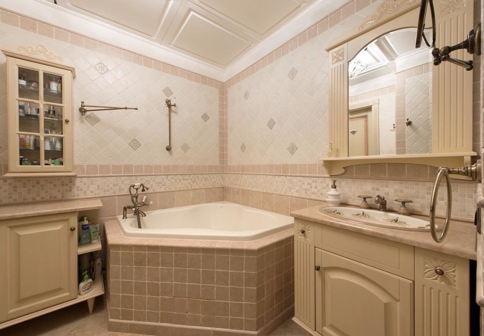 Immagine di una stanza da bagno padronale chic di medie dimensioni con ante con bugna sagomata, ante beige, vasca ad angolo, piastrelle in pietra, pavimento in marmo, top in marmo, pareti rosa, lavabo da incasso e piastrelle beige