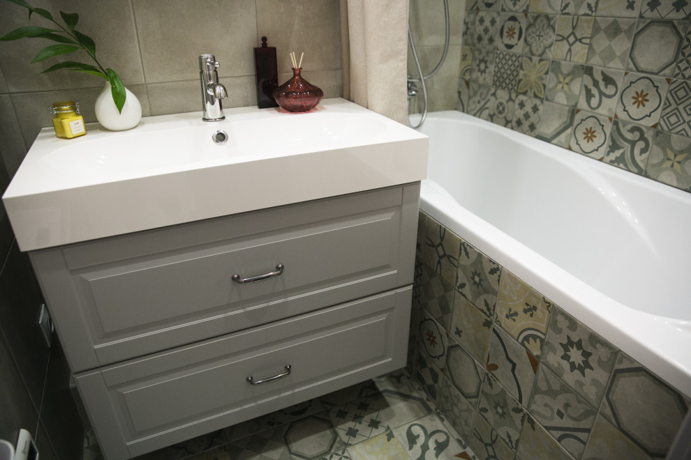 Photo of a small scandi ensuite bathroom in Saint Petersburg with raised-panel cabinets, grey cabinets, a submerged bath, a shower/bath combination, beige tiles, porcelain tiles, beige walls, porcelain flooring, a built-in sink, solid surface worktops, beige floors, white worktops, a single sink and a floating vanity unit.