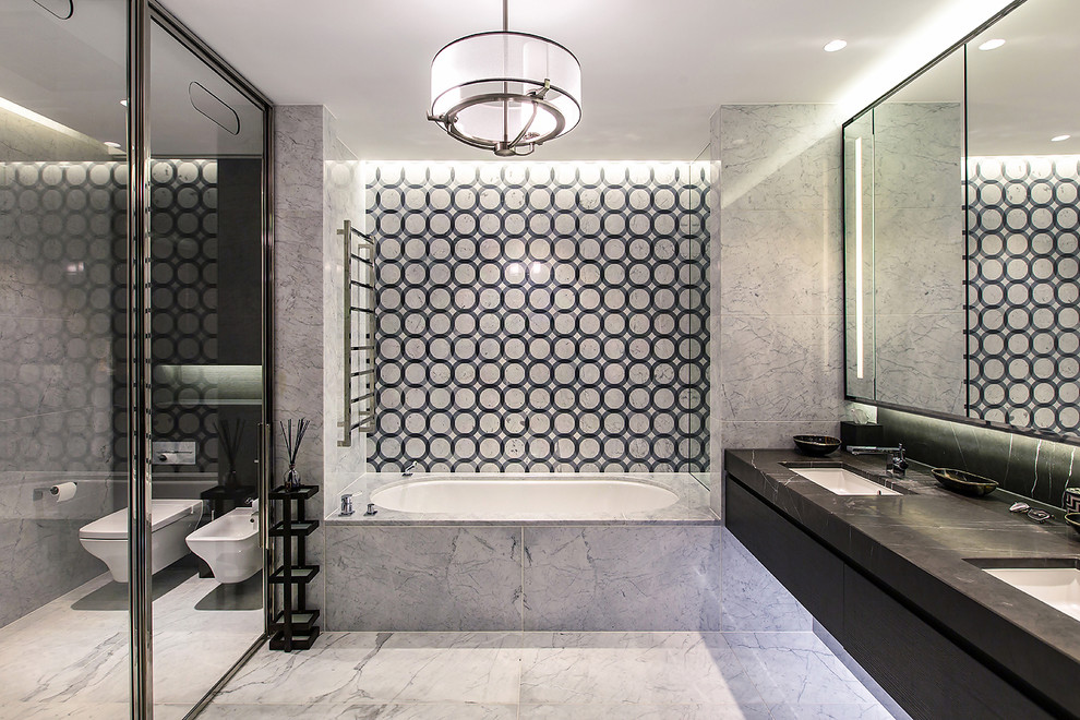 Cette image montre une salle de bain principale design avec une baignoire encastrée, WC suspendus, un lavabo encastré, un sol gris, un placard à porte plane, des portes de placard noires et des toilettes cachées.