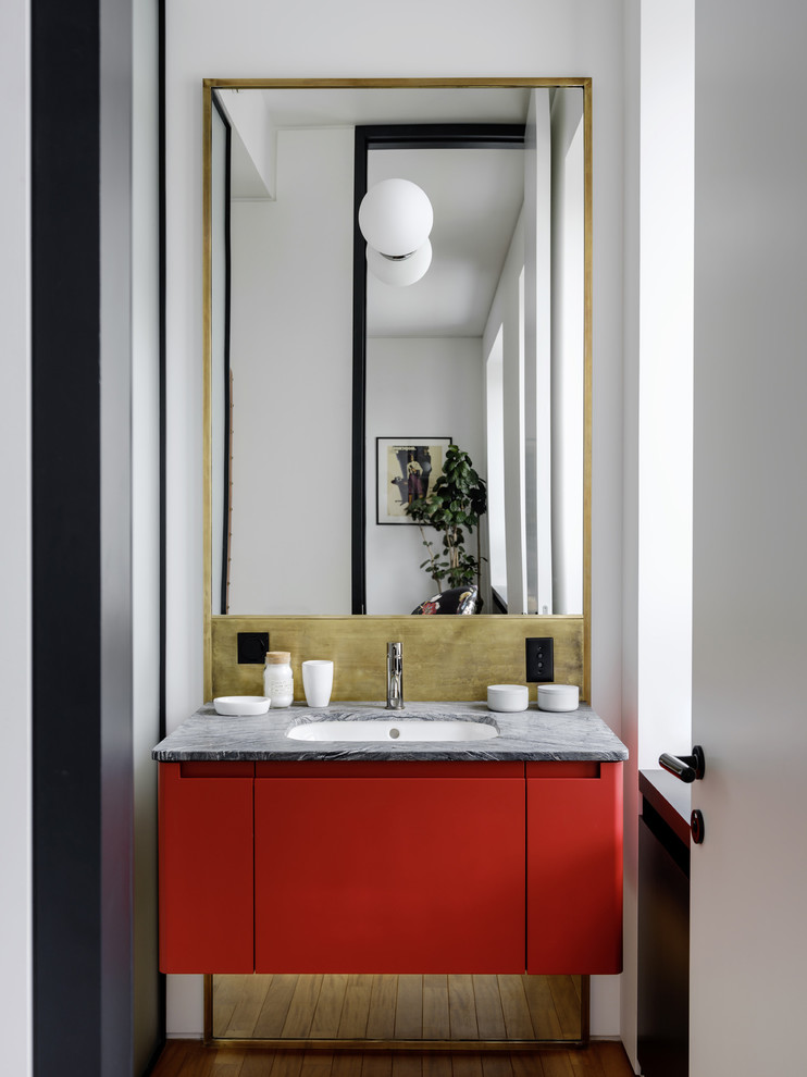 Ejemplo de cuarto de baño actual con paredes blancas, suelo de madera en tonos medios, suelo marrón, armarios con paneles lisos, puertas de armario rojas, lavabo bajoencimera, encimeras grises y espejo con luz