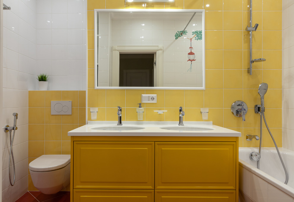 На фото: детская ванная комната в стиле неоклассика (современная классика) с фасадами с выступающей филенкой, желтыми фасадами, ванной в нише, душем над ванной, инсталляцией, белой плиткой, желтой плиткой, разноцветными стенами, врезной раковиной и белой столешницей с