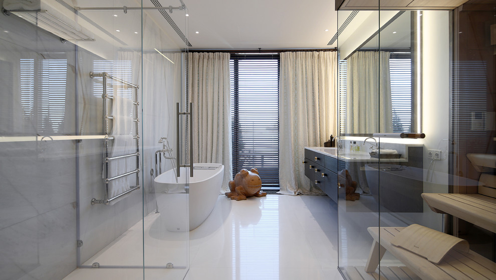 Modern inredning av ett en-suite badrum, med släta luckor, svarta skåp, ett fristående badkar, en kantlös dusch, vita väggar och ett undermonterad handfat