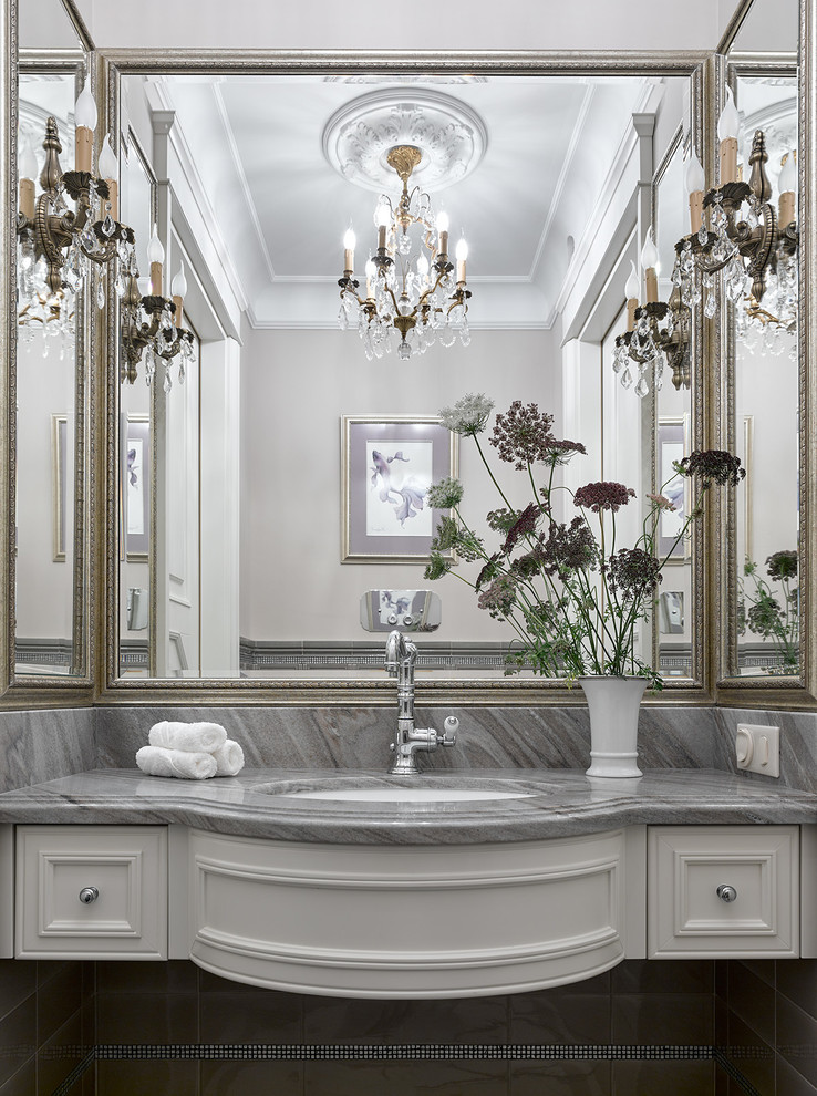 Modelo de cuarto de baño tradicional con armarios con paneles empotrados, puertas de armario blancas, lavabo bajoencimera, baldosas y/o azulejos grises, baldosas y/o azulejos de cerámica, encimera de mármol, paredes grises y espejo con luz