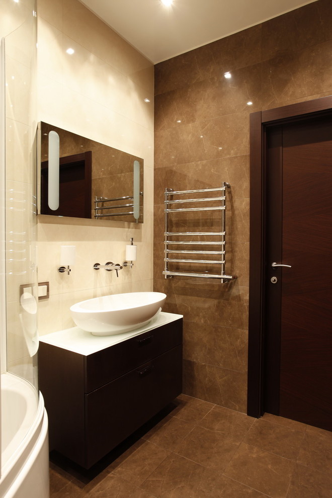 Свежая идея для дизайна: главная ванная комната среднего размера в современном стиле с плоскими фасадами, темными деревянными фасадами, угловой ванной, душем над ванной, инсталляцией, коричневой плиткой, керамической плиткой, бежевыми стенами, полом из керамогранита, раковиной с пьедесталом, коричневым полом, душем с раздвижными дверями и белой столешницей - отличное фото интерьера