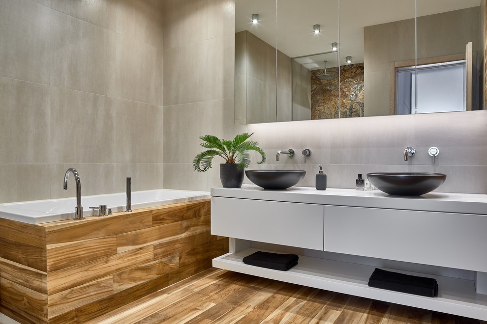 Идея дизайна: главная ванная комната в современном стиле с плоскими фасадами, белыми фасадами, серой плиткой, настольной раковиной, коричневым полом, накладной ванной и серыми стенами