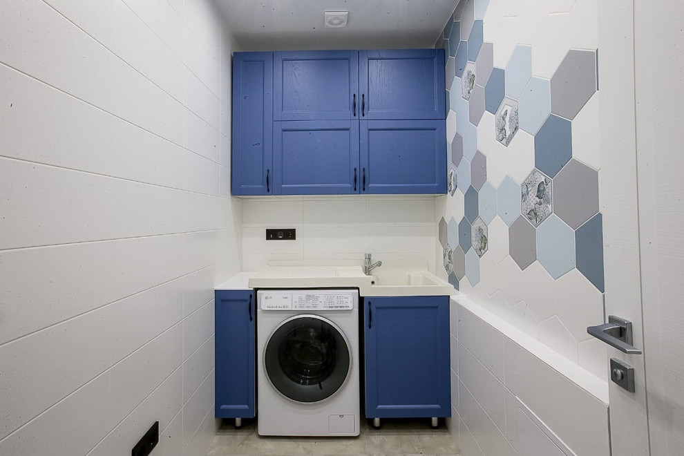 Modelo de lavadero actual pequeño con armarios con paneles con relieve, puertas de armario azules, paredes blancas, suelo de baldosas de porcelana y suelo beige