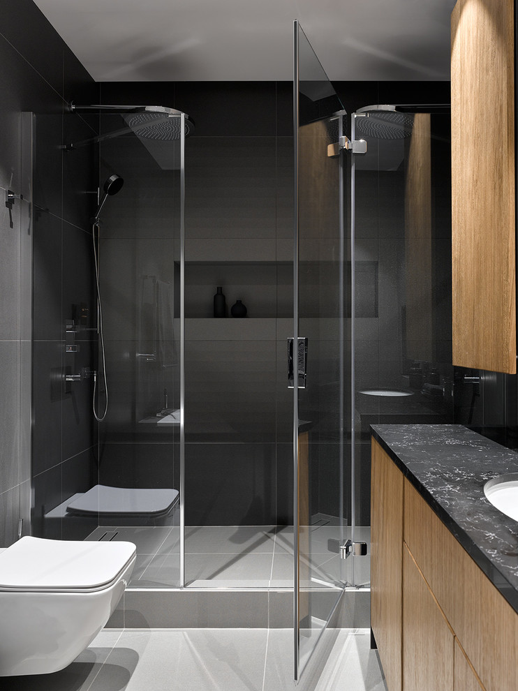 Immagine di una stanza da bagno con doccia contemporanea con ante lisce, ante in legno scuro, piastrelle grigie, lavabo sottopiano, pavimento grigio, top nero, doccia alcova e WC sospeso