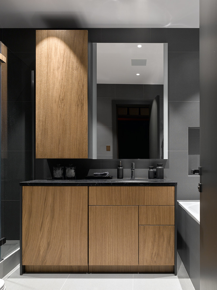 Idée de décoration pour une salle de bain principale design en bois brun avec un placard à porte plane, une baignoire en alcôve, un carrelage gris, un lavabo encastré, un sol gris et un plan de toilette noir.