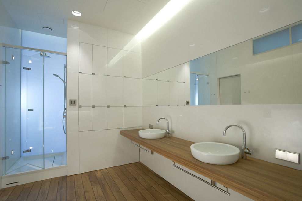 Bild på ett mellanstort funkis en-suite badrum, med släta luckor, vita skåp, ett fristående badkar, en dusch i en alkov, en vägghängd toalettstol, vit kakel, stenhäll, vita väggar, mellanmörkt trägolv, ett nedsänkt handfat och träbänkskiva