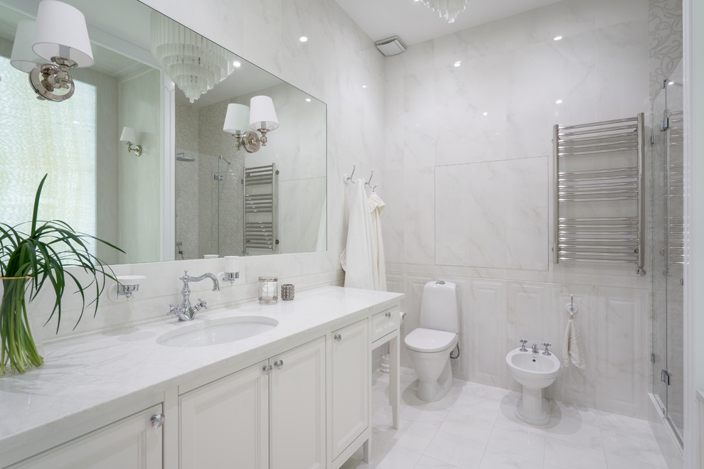 На фото: главная ванная комната в стиле неоклассика (современная классика) с фасадами с утопленной филенкой, белыми фасадами, биде, белой плиткой, врезной раковиной, белым полом и белой столешницей с