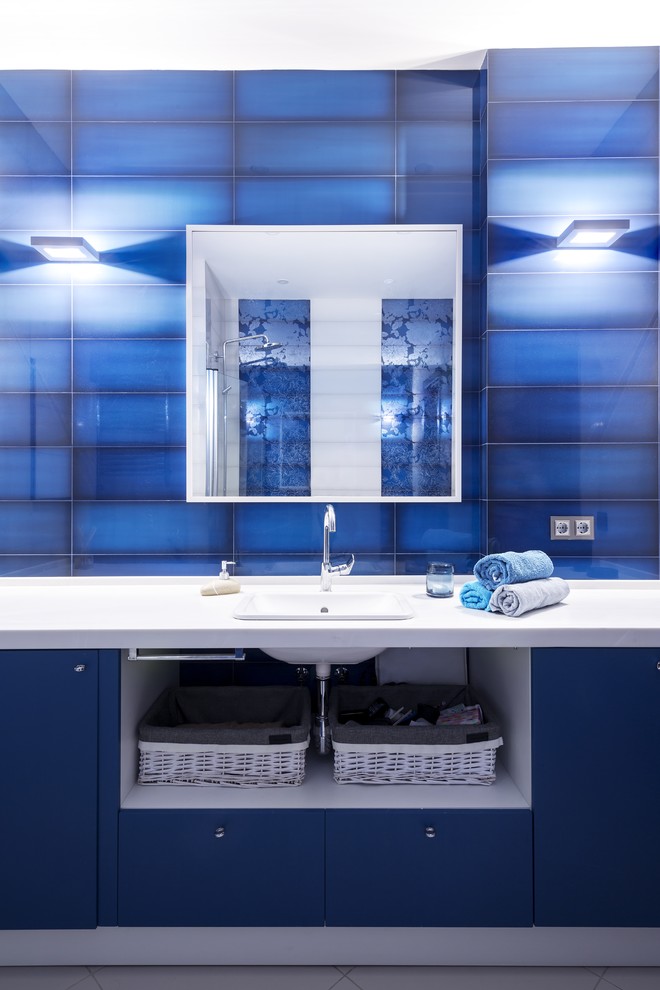 モスクワにある中くらいなコンテンポラリースタイルのおしゃれなマスターバスルーム (フラットパネル扉のキャビネット、青いキャビネット、大型浴槽、壁掛け式トイレ、青いタイル、セラミックタイル、青い壁、セラミックタイルの床、オーバーカウンターシンク、人工大理石カウンター、グレーの床、白い洗面カウンター) の写真