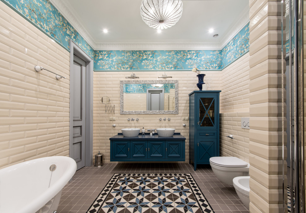 Пример оригинального дизайна: большая ванная комната в классическом стиле с синими фасадами, ванной на ножках, душем в нише, инсталляцией, бежевой плиткой, плиткой кабанчик, синими стенами, полом из керамической плитки, столешницей из искусственного камня, душем с распашными дверями, настольной раковиной, разноцветным полом и акцентной стеной