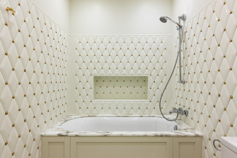 На фото: главная ванная комната в стиле неоклассика (современная классика) с полновстраиваемой ванной, душем над ванной, белой плиткой, белыми стенами, бежевыми фасадами и открытым душем