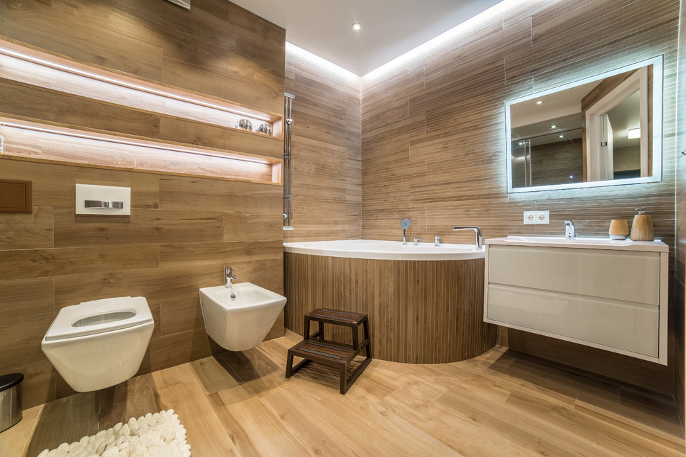 Modern inredning av ett vit vitt badrum med dusch, med släta luckor, vita skåp, ett hörnbadkar, en vägghängd toalettstol, beige kakel, ett integrerad handfat och beiget golv