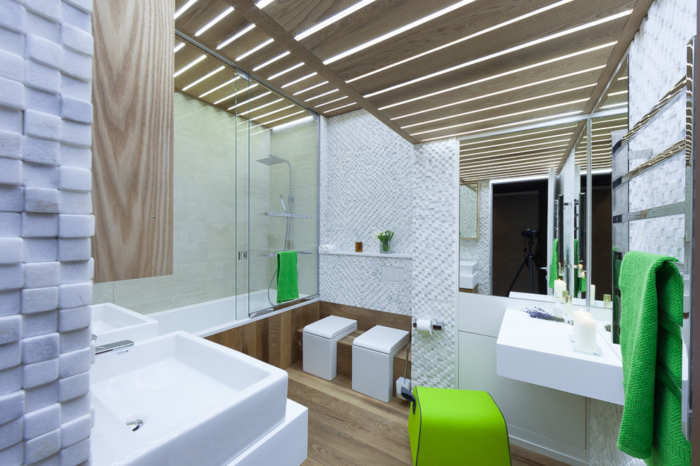 Cette photo montre une salle de bain principale bord de mer en bois brun de taille moyenne avec une baignoire encastrée, un combiné douche/baignoire, un carrelage blanc, un carrelage de pierre, un mur blanc, un sol en bois brun et un plan de toilette en surface solide.