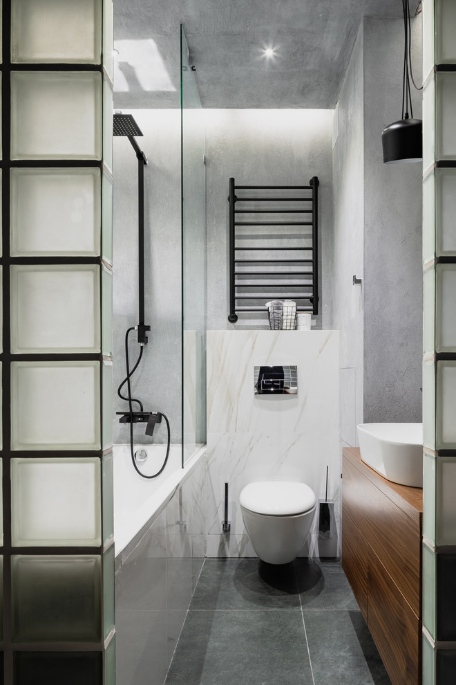 Modelo de cuarto de baño principal contemporáneo con bañera empotrada, combinación de ducha y bañera, lavabo sobreencimera, sanitario de pared, paredes grises y suelo gris