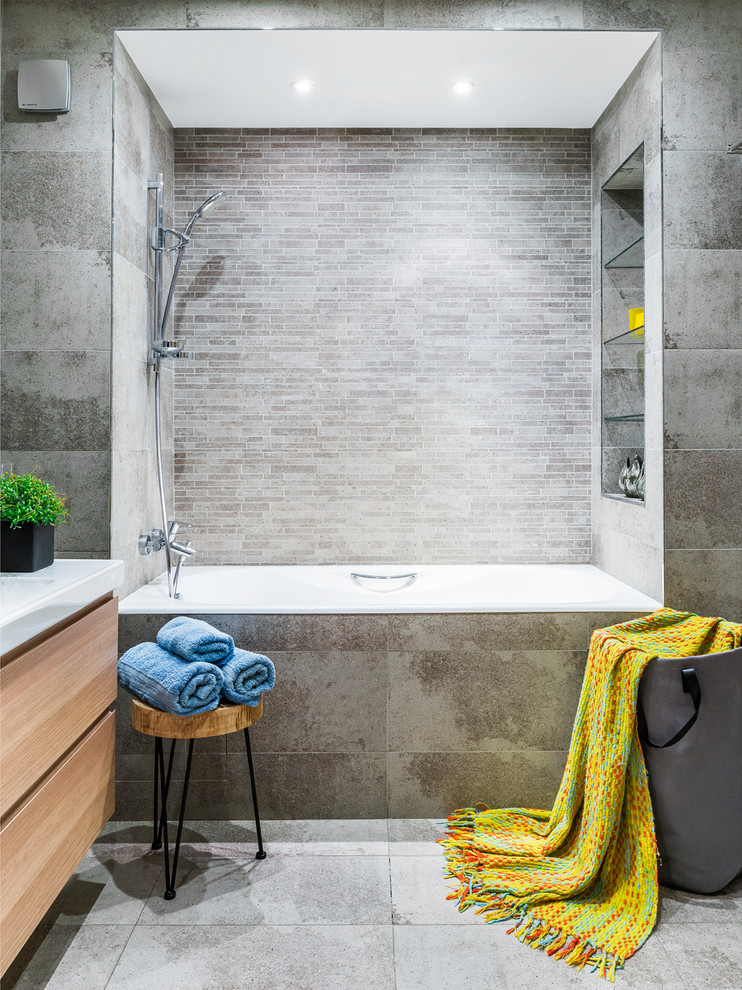 Idée de décoration pour une salle de bain principale design en bois clair avec un placard à porte plane, une baignoire en alcôve, un combiné douche/baignoire, un carrelage gris, un lavabo intégré et un sol gris.