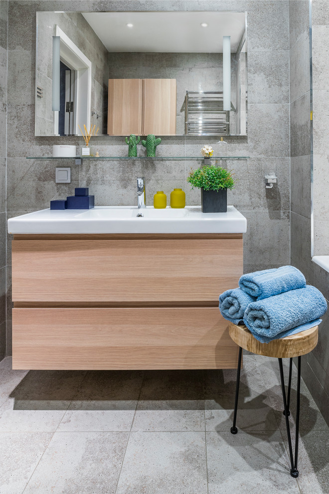 Inredning av ett modernt en-suite badrum, med släta luckor, skåp i ljust trä, grå kakel, ett integrerad handfat och grått golv