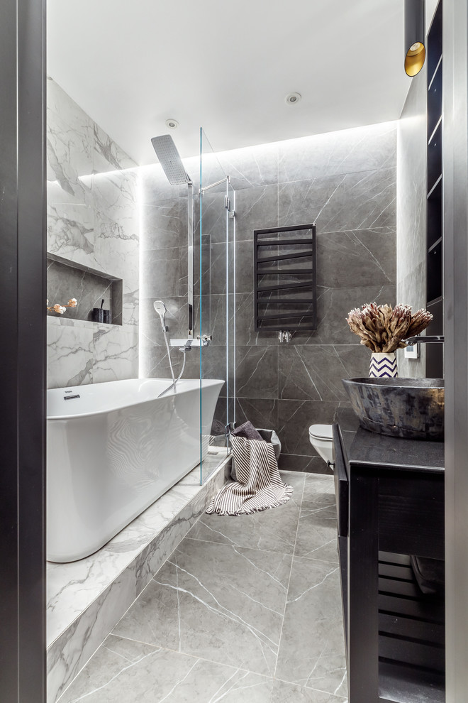 Идея дизайна: главная ванная комната среднего размера в современном стиле с плоскими фасадами, черными фасадами, отдельно стоящей ванной, инсталляцией, керамогранитной плиткой, полом из керамогранита, настольной раковиной, серым полом, душем над ванной, белой плиткой и серой плиткой