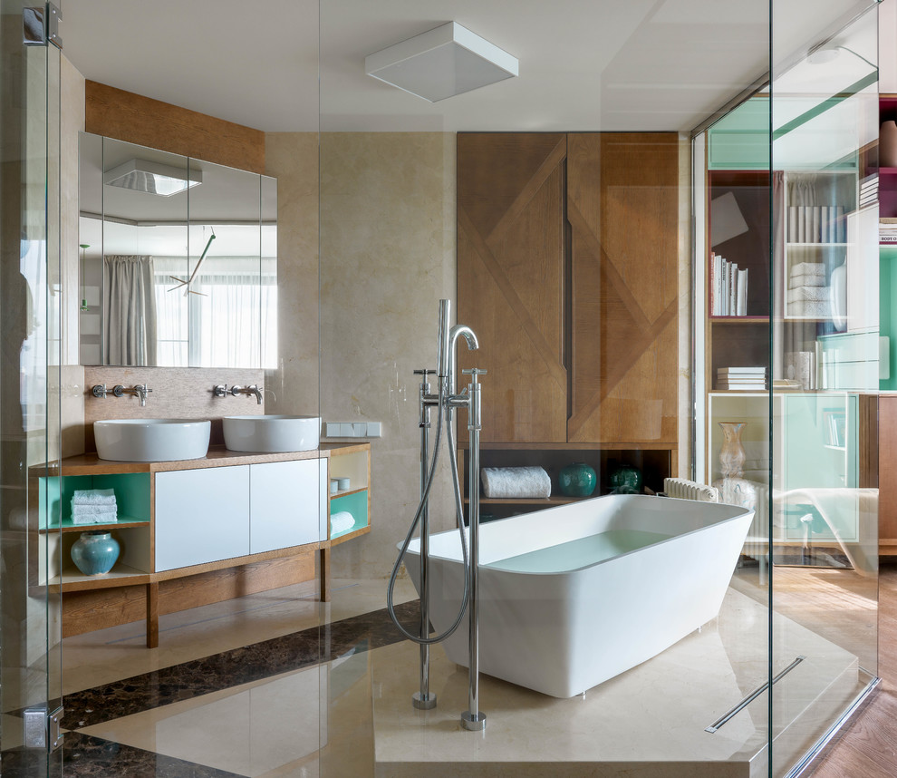 На фото: главная ванная комната в современном стиле с плоскими фасадами, белыми фасадами, отдельно стоящей ванной, бежевой плиткой, настольной раковиной, бежевым полом и коричневой столешницей