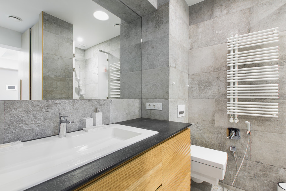 Idée de décoration pour une salle de bain nordique en bois clair de taille moyenne avec WC suspendus, un carrelage gris, des carreaux de porcelaine, un sol en carrelage de porcelaine, un plan de toilette en quartz modifié et un lavabo posé.