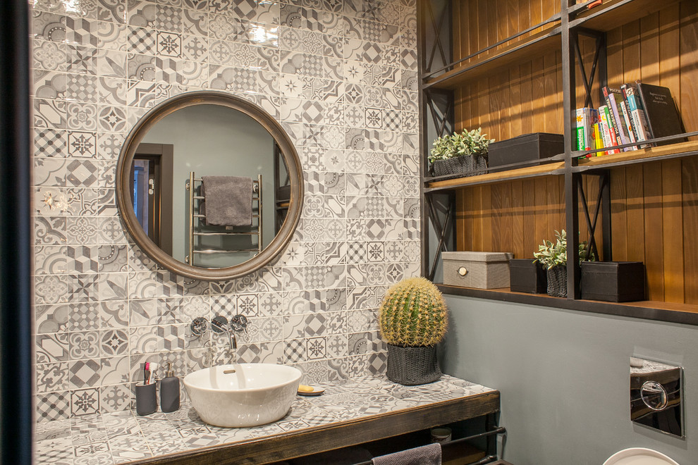 Modelo de cuarto de baño urbano con sanitario de pared, baldosas y/o azulejos grises, paredes grises, lavabo sobreencimera y encimera de azulejos