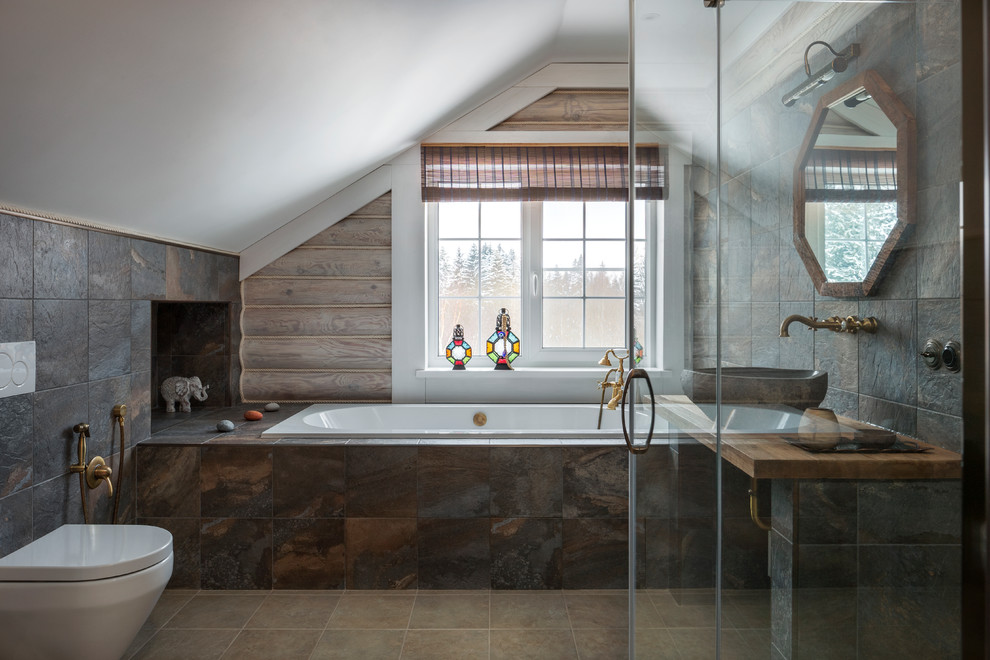 На фото: главная ванная комната в деревянном доме в стиле рустика с накладной ванной, инсталляцией, коричневой плиткой, коричневыми стенами, настольной раковиной, столешницей из дерева, бежевым полом и коричневой столешницей с