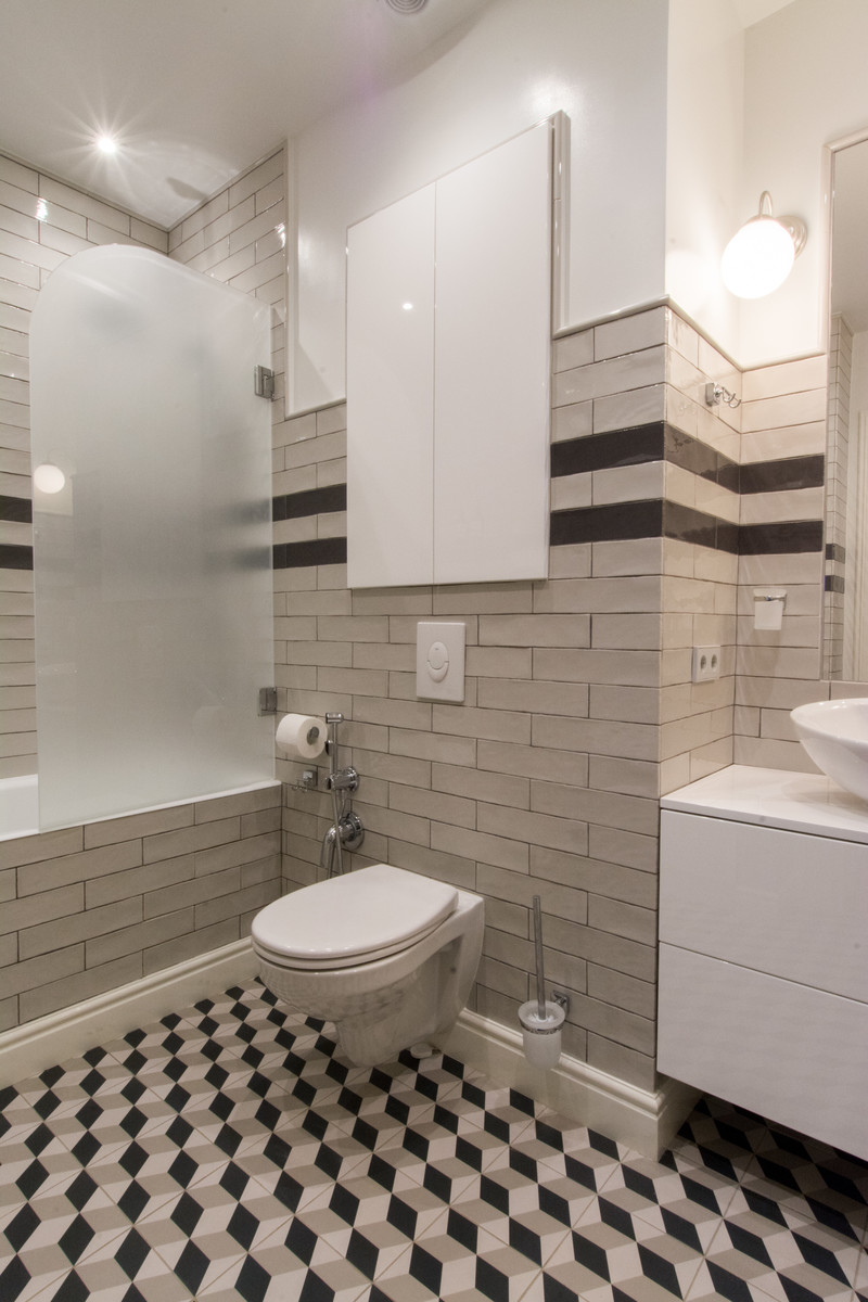 На фото: главная ванная комната в современном стиле с плоскими фасадами, белыми фасадами, ванной в нише, душем над ванной, инсталляцией, бежевой плиткой, белыми стенами, настольной раковиной и разноцветным полом с