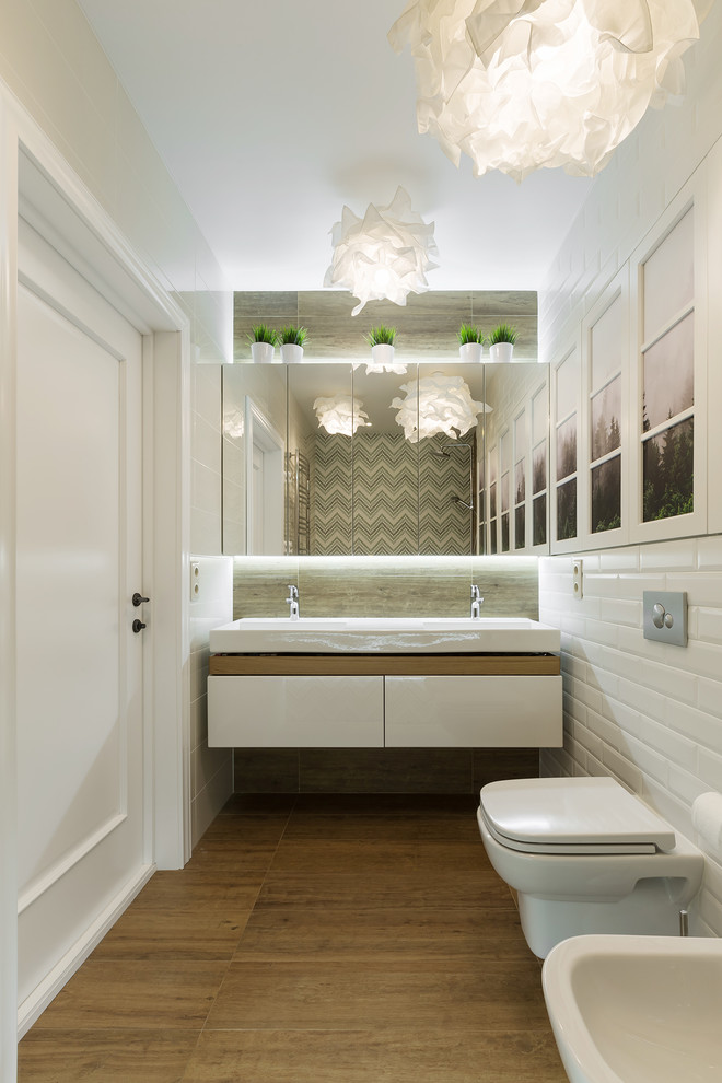 This is an example of a contemporary shower room bathroom in Yekaterinburg with a wall mounted toilet, porcelain flooring, flat-panel cabinets, white cabinets, an alcove shower, grey tiles, white tiles, metro tiles, an integrated sink and brown floors.